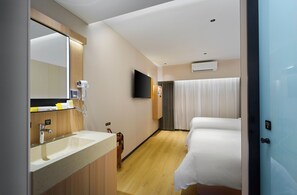 Una habitación de hotel con baño, cama, televisor y ventana con cortinas.
