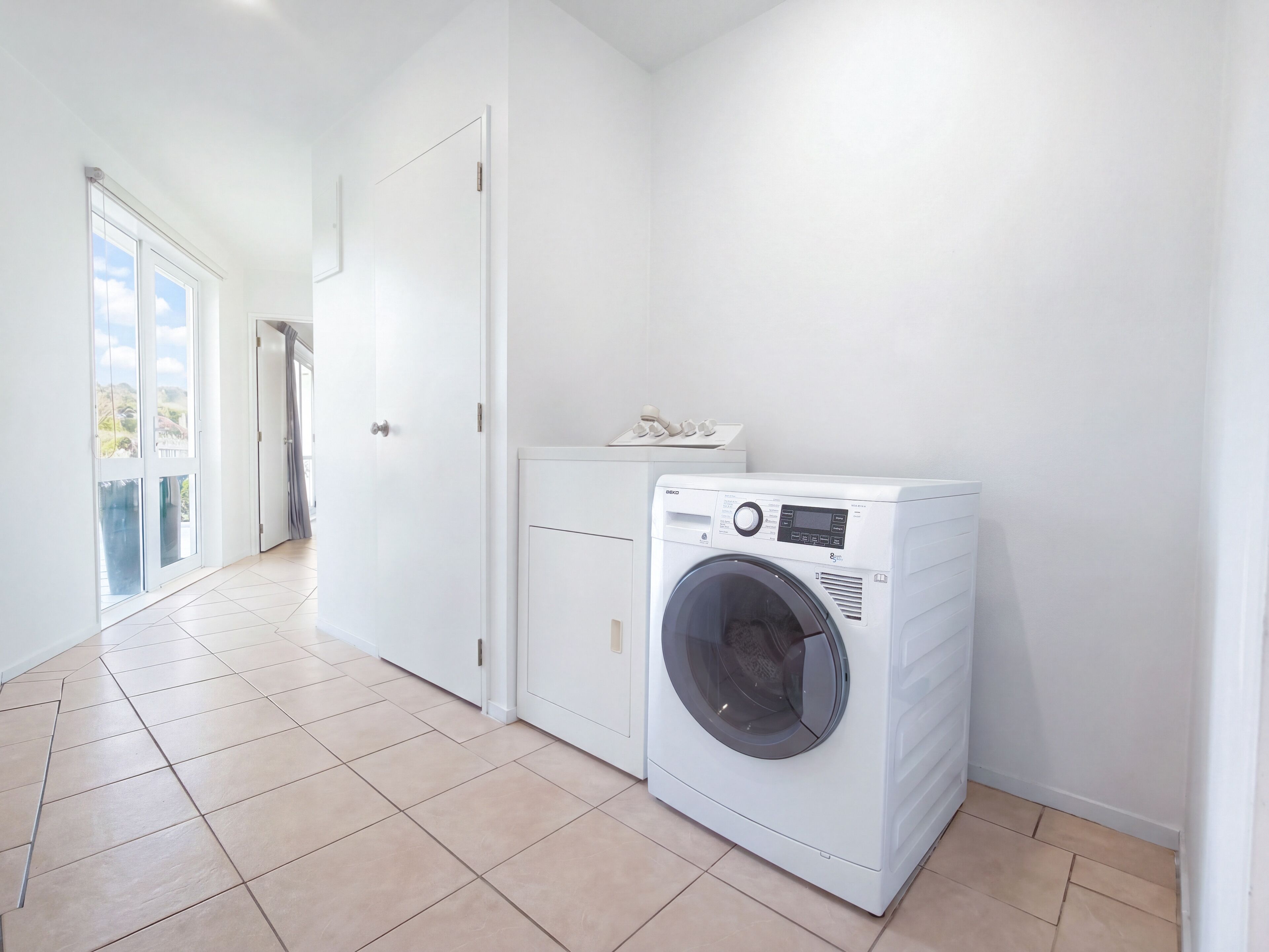 A laundry room with a front-loading washing machine, a door, and a tiled floor.