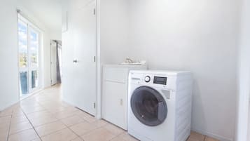 A laundry room with a front-loading washing machine, a door, and a tiled floor.
