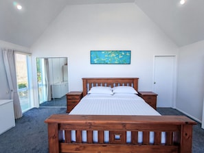 A bedroom with a wooden bed, a nightstand, a dresser, a mirror, and a painting on the wall.