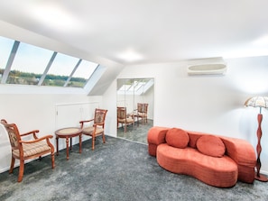 Una habitaci ón con techo inclinado, un sofá, una mesa de comedor con sillas y un amplio ventanal con vistas al exterior.