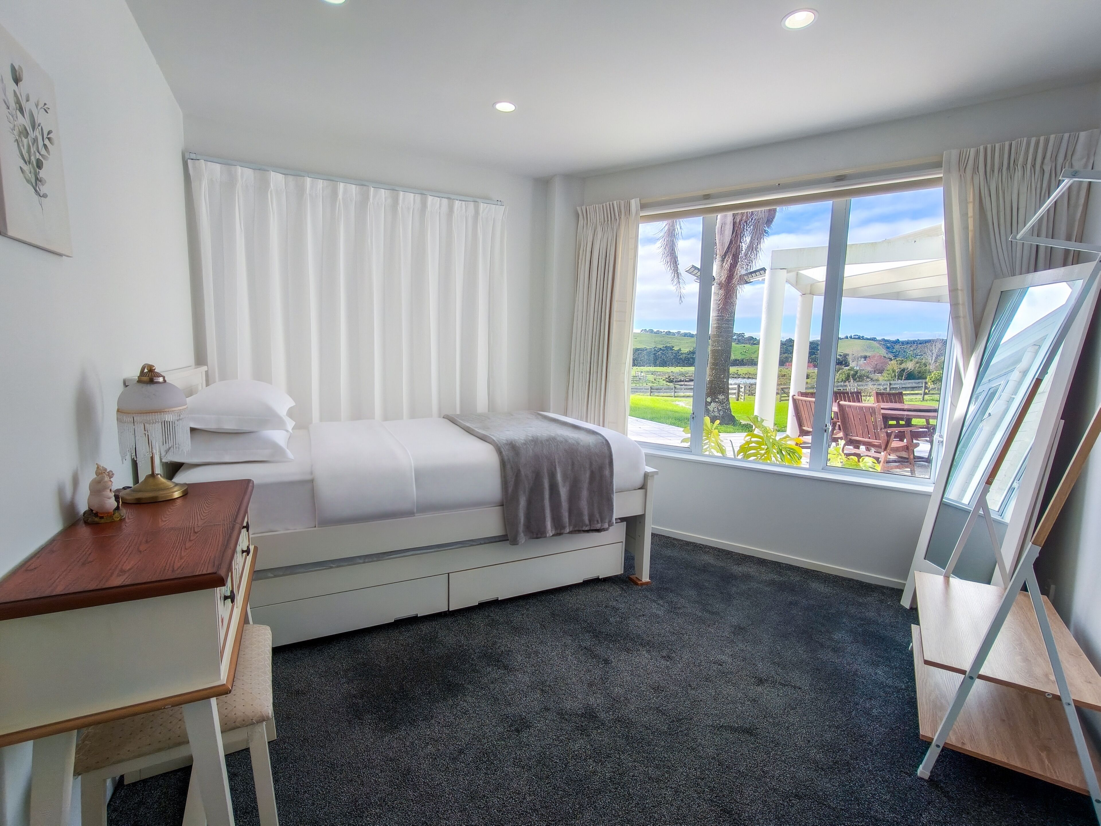 Une chambre à coucher comprenant un lit, un bureau, une chaise, une fenêtre avec des rideaux et une vue sur l’extérieur.