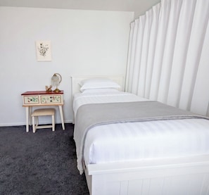 A bedroom with a bed, a nightstand with a lamp, a chair, and a wall-mounted picture.