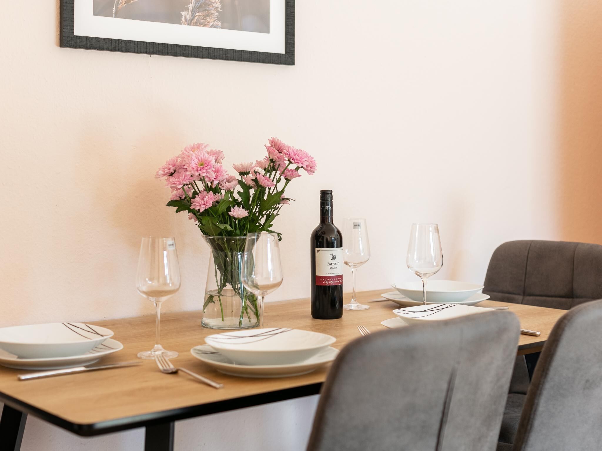 Una mesa de comedor dispuesta con platos, cubiertos, una botella de vino y un florero con flores.