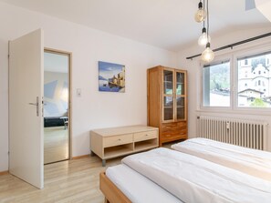 A bedroom with a bed, a wooden cabinet, a painting, and a window with a view of buildings. - Two penthouse apartments in the center. (Hopfgarten im Brixental)