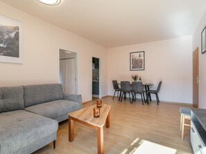 A modern living room with a grey sofa, wooden coffee table, and a dining area with chairs and a table. - Two penthouse apartments in the center. (Hopfgarten im Brixental)