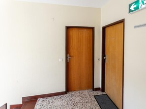 A hallway with two wooden doors, a tiled floor, and a green emergency exit sign. - Two penthouse apartments in the center. (Hopfgarten im Brixental)