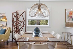 Un espace repas avec une table en verre, des chaises blanches, un vase bleu, un paravent en bois aux motifs géométriques et un luminaire suspendu.