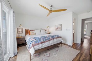 Ein Schlafzimmer mit einem Bett, einem Deckenventilator, einem Nachttisch, einer Lampe und einer Tür zu einem anderen Raum.
