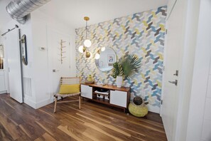Ein modernes Interieur mit einer Wand mit geometrischem Muster, einer Holzbank, einem Konsolentisch und einer Topfpflanze.