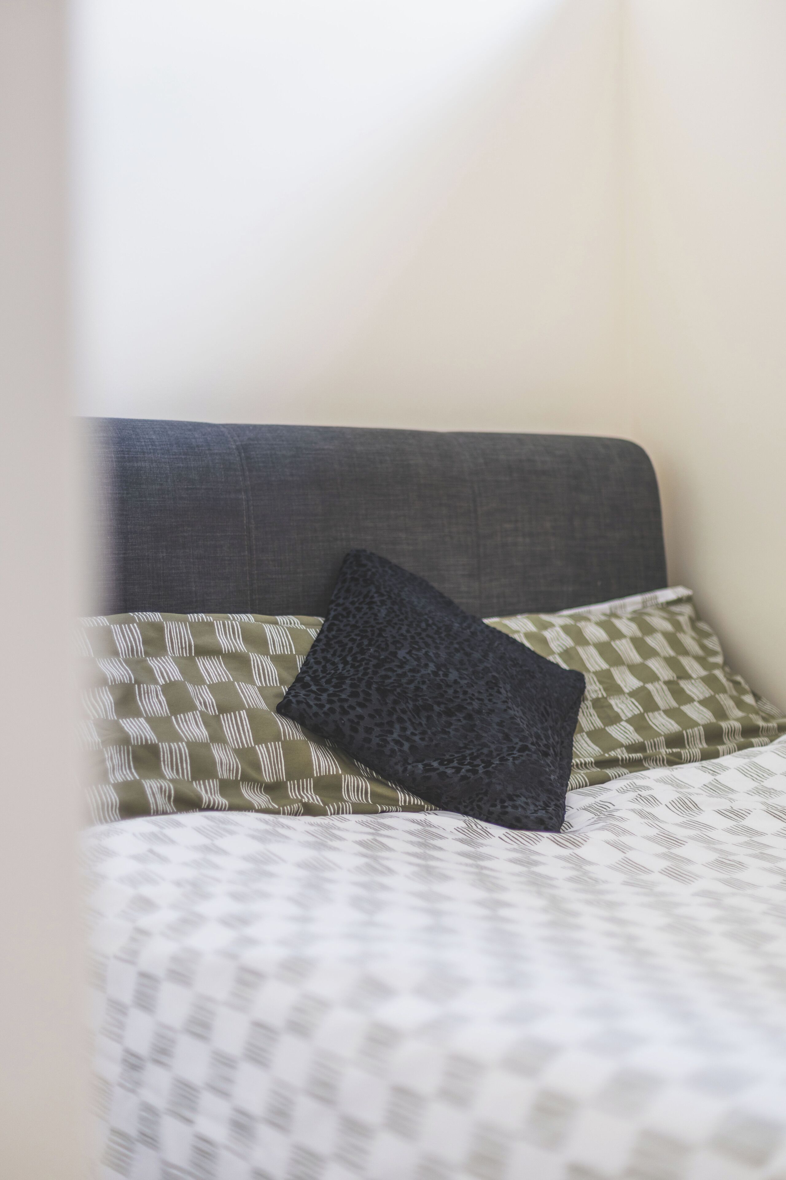 Una cama con un edredón estampado, un cabecero gris y dos almohadas con diseños diferentes.