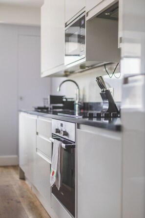 A modern kitchen with a built-in oven, microwave, and stainless steel appliances. - Stylish 2BR | Fast Links to Central London (Croydon)