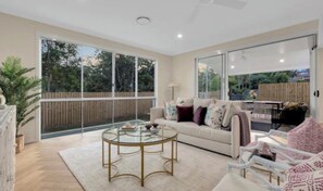 A spacious living area with a glass coffee table, a sofa with cushions, and a view of the outdoors through large sliding glass doors. - WELCOME HOME (Chapel Hill)