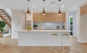 A modern kitchen with a central island, pendant lighting, and a staircase in the background. - WELCOME HOME (Chapel Hill)