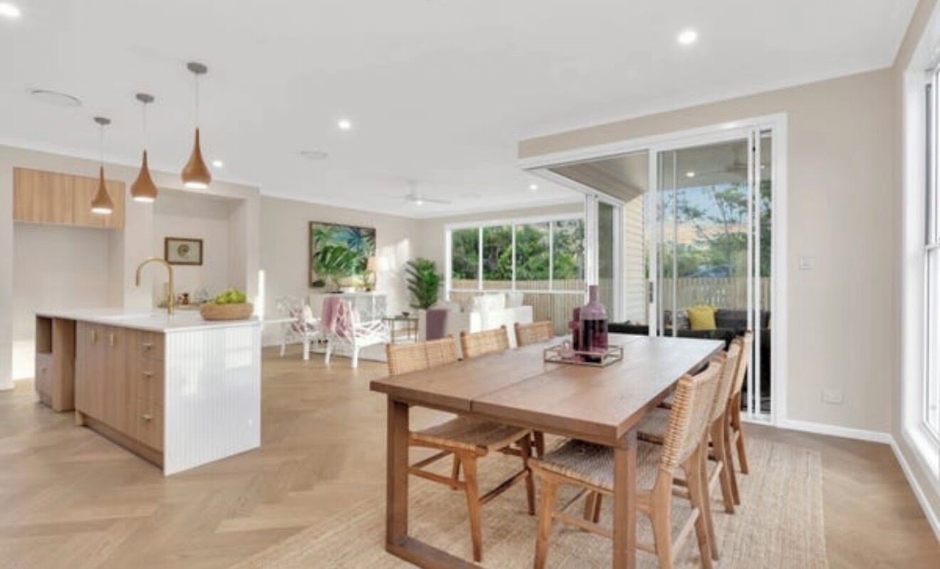 A modern kitchen with a central island, dining area with a wooden table and chairs, and a sliding glass door leading to an outdoor area.