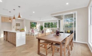A modern kitchen with a central island, dining area with a wooden table and chairs, and a sliding glass door leading to an outdoor area. - WELCOME HOME (Chapel Hill)