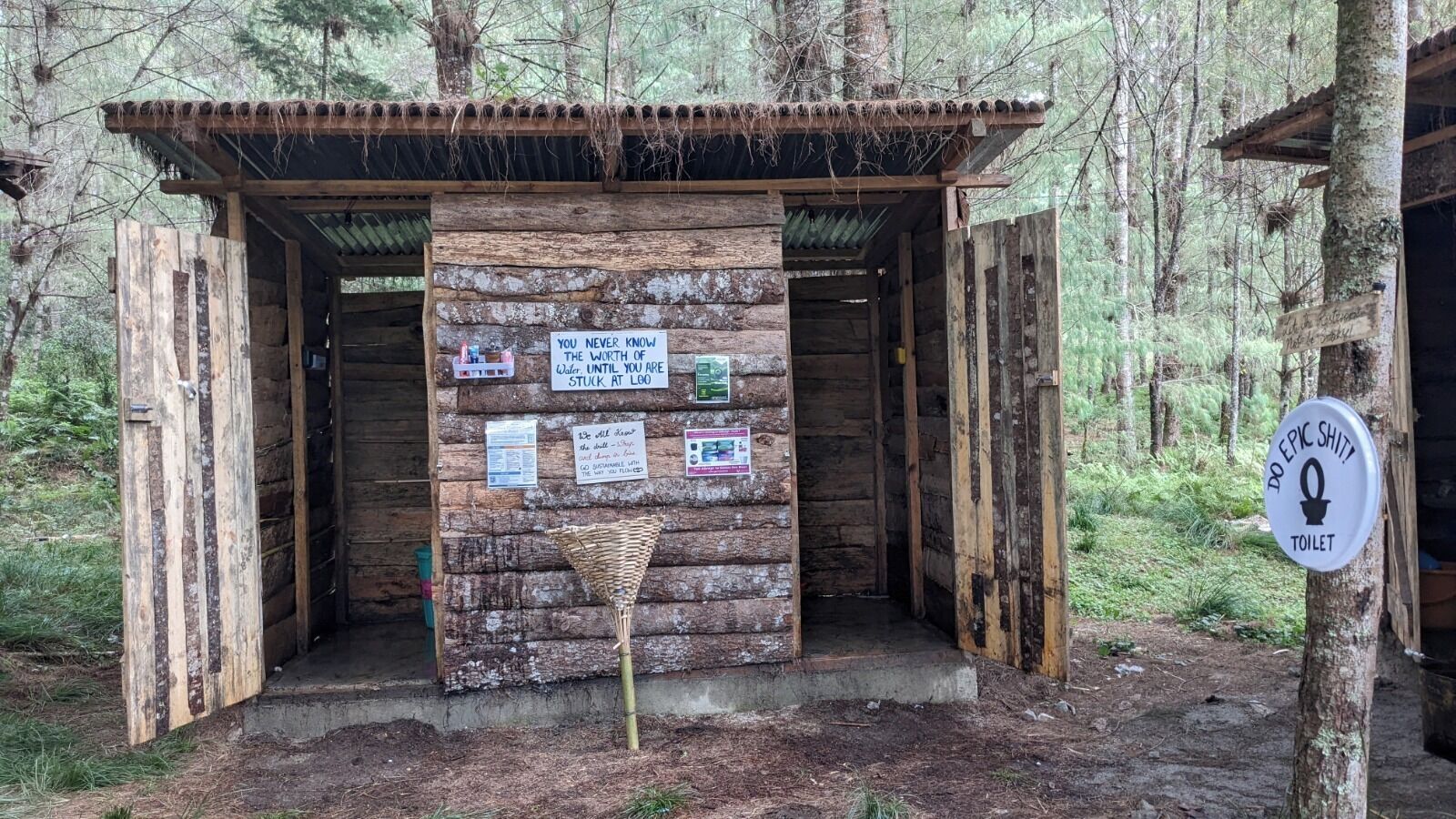 Una estructura de madera rústica con un cartel que muestra varios avisos y una señalización de baño.