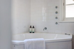 Un baño con una bañera blanca, dos botellas de champú y un ventanal.