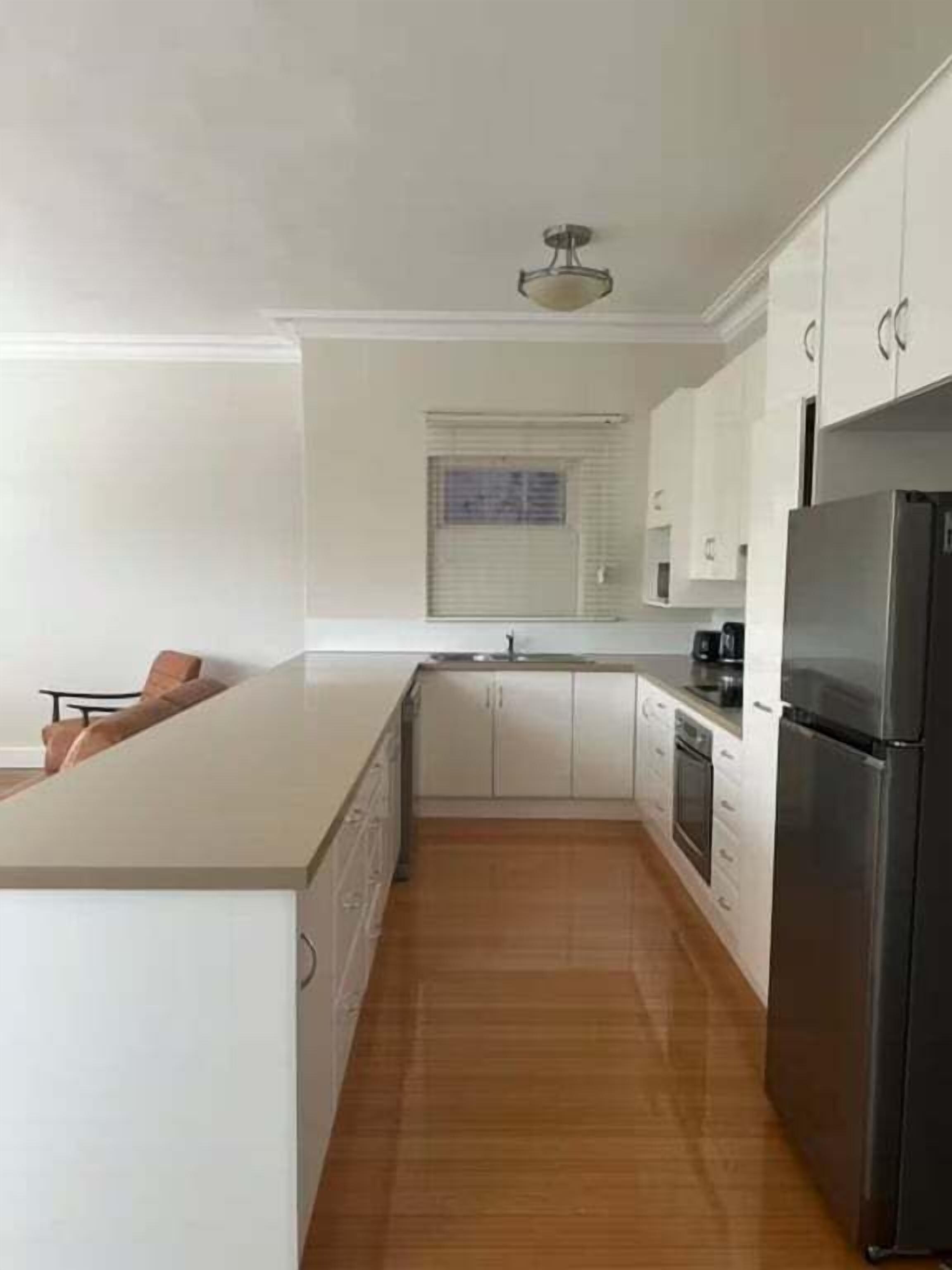 A kitchen with white cabinets, a stainless steel refrigerator, and a wooden floor.