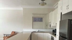 A kitchen with white cabinets, a stainless steel refrigerator, and a wooden floor. - City Loft | Stylish CBD Stay + River Walks (Rockhampton)