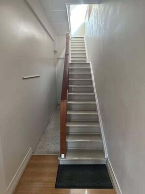 Een smalle gang met houten leuning en vloerbedekking, die leidt naar een trap.