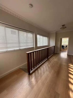 A hallway with wooden flooring, a railing, and large windows with blinds.