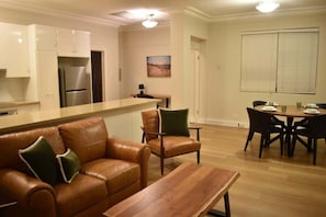 A modern kitchen with a built-in refrigerator, a dining area with a wooden table and chairs, and a leather sofa with cushions.