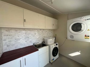 A laundry room with a washing machine, a sink, and a tiled backsplash.