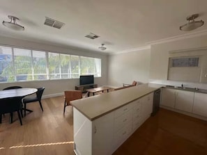 Een ruime keuken met een centraal eiland, een eethoek met stoelen en een groot raam dat zorgt voor veel daglicht.