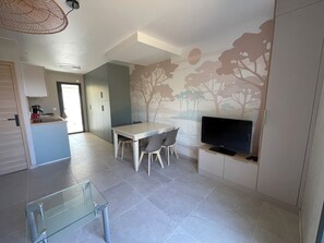 A modern kitchen with a dining area, a glass table, and a flat-screen TV mounted on a cabinet. - Vrbo Property (La Plaine-sur-Mer)