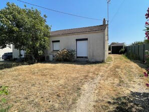 A single-story building with a tiled roof, a closed garage door, and a small air conditioning unit. - Vrbo Property (La Plaine-sur-Mer)