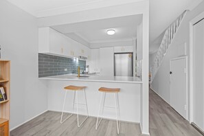 Ett modernt kök med en central köksö, två barstolar och ett kylskåp i rostfritt stål.