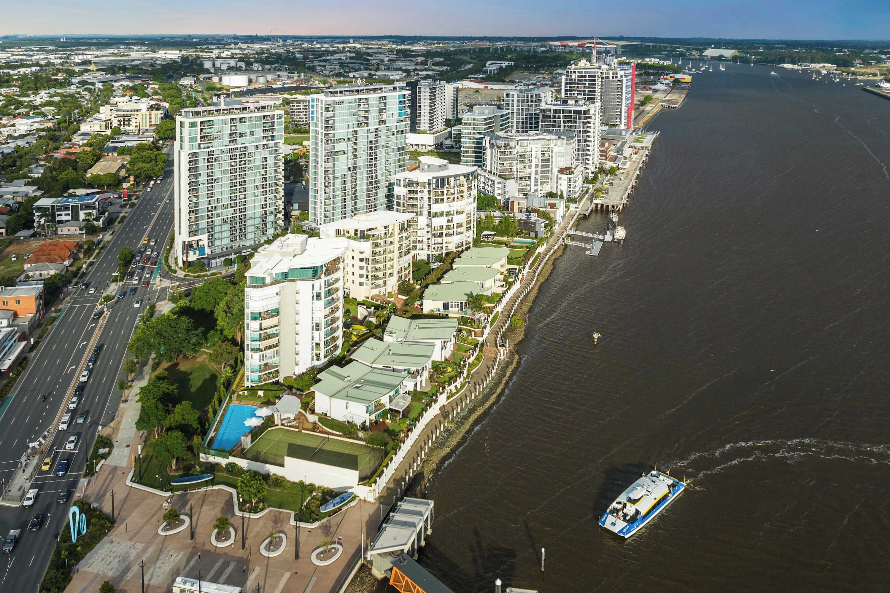 Ein Hochhaus-Wohnkomplex mit mehreren Balkonen, einer Uferpromenade und einem Fluss mit einem Boot.