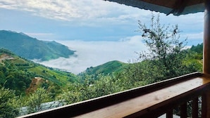 A view from a wooden balcony overlooking a lush valley with a body of water and mountains in the distance. - Co House Ta Xua (Ta Xua)