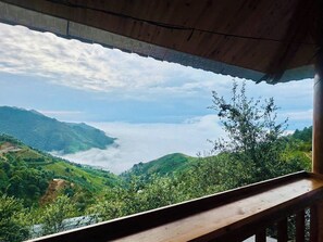 A view from a wooden balcony overlooking a lush valley with a body of water and mountains in the distance.