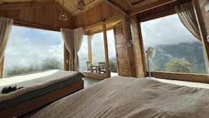 A wooden cabin with a bed and a table, large windows, and a view of the mountains. - Co House Ta Xua (Ta Xua)