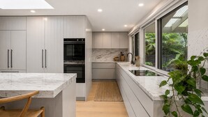 Cozinha moderna com armários brancos, forno embutido, bancada de mármore e janela com vista para o verde.