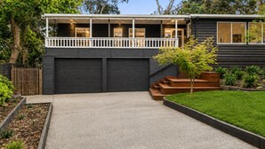 Uma casa moderna de dois andares com varanda coberta, garagem e um jardim bem cuidado.