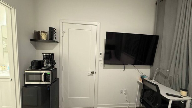 Une chambre d’hôtel compacte comprenant un coin cuisine, un téléviseur à écran plat, un lit et un bureau avec une chaise.