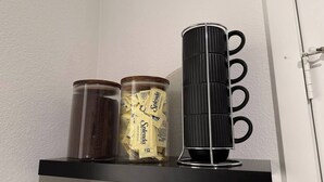 Une étagère avec trois récipients : un bocal en verre transparent, un bocal en plastique transparent avec une étiquette, et un récipient cylindrique noir avec des anneaux.