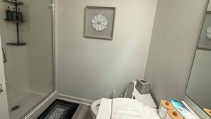 Une salle de bain avec une douche, des toilettes et un lavabo. Un tableau encadré est accroché au mur, et il y a un porte-serviettes avec des serviettes.