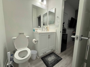 A bathroom with a toilet, sink, mirror, and cabinets.