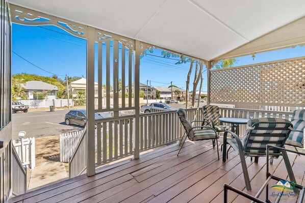 A covered outdoor area with a wooden deck, chairs, and a view of the street.