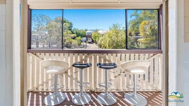 A balcony with three bar stools and a view of a residential area through a large window. - City Cottage (Rockhampton)