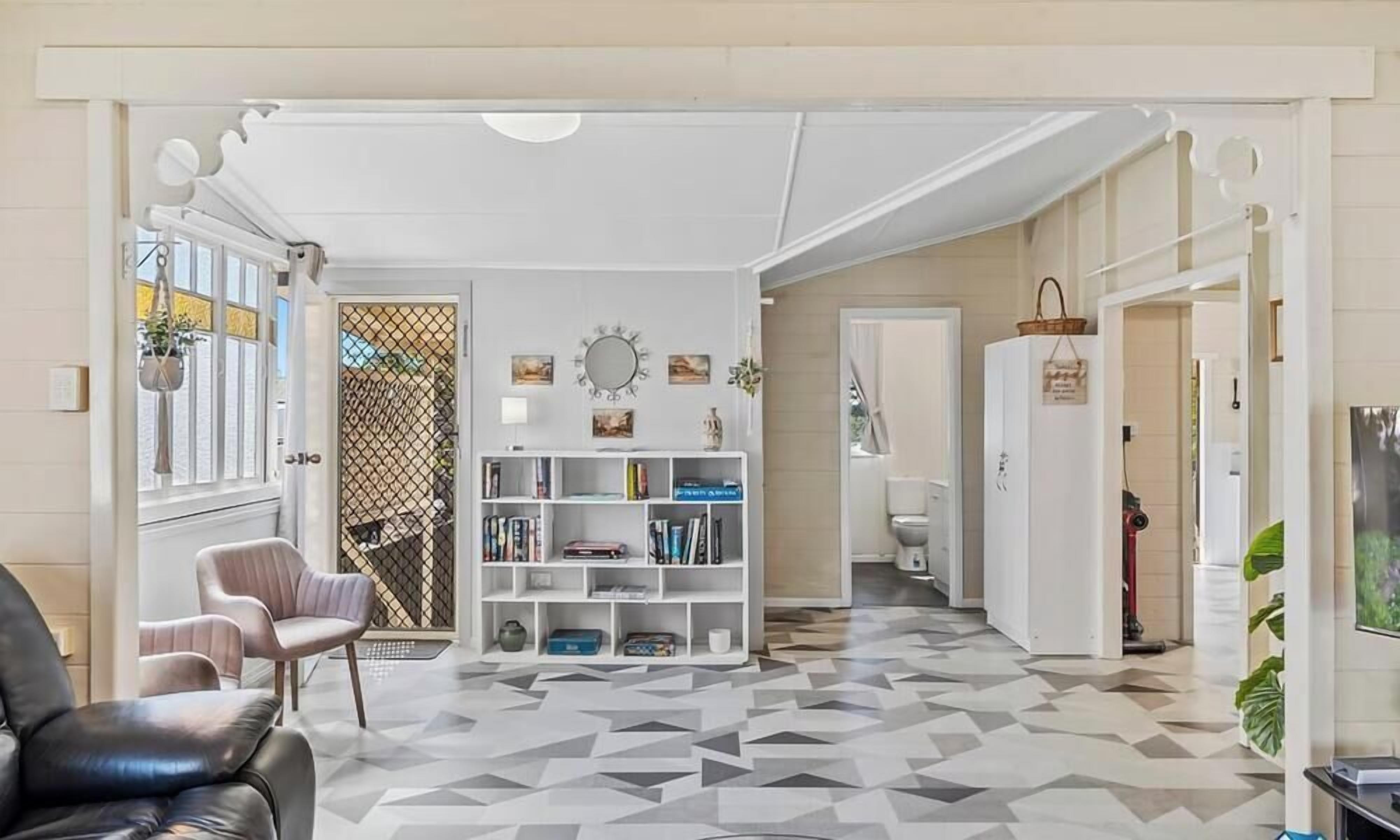 A hallway with a geometric patterned floor, a white console table with books, a black leather chair, and a white door leading to another room.