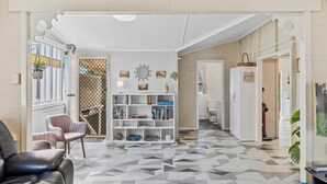 A hallway with a geometric patterned floor, a white console table with books, a black leather chair, and a white door leading to another room. - City Cottage (Rockhampton)