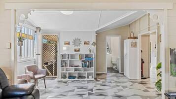A hallway with a geometric patterned floor, a white console table with books, a black leather chair, and a white door leading to another room.