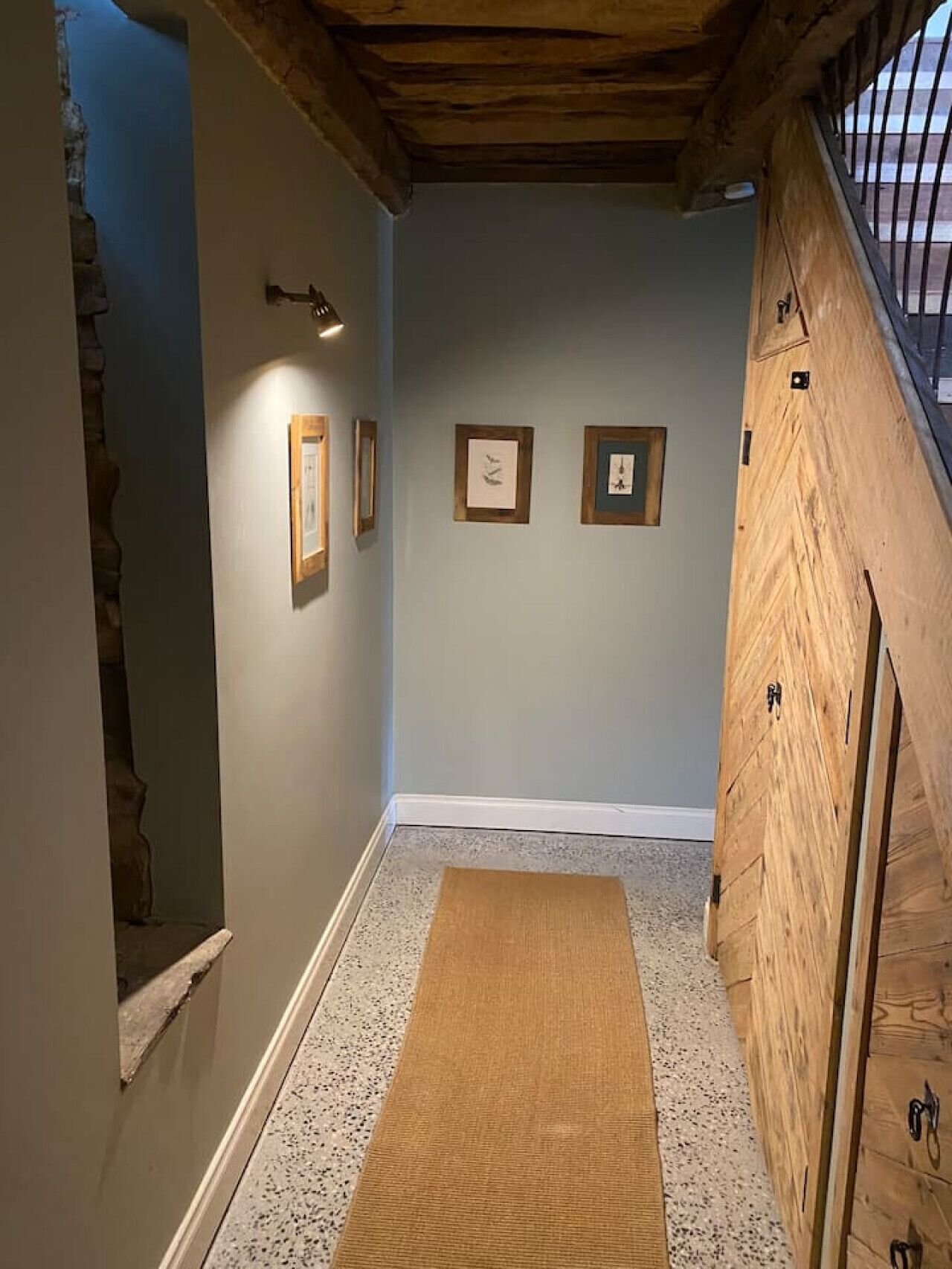 Un couloir avec un escalier en bois, un tapis et des tableaux encadrés accrochés au mur.