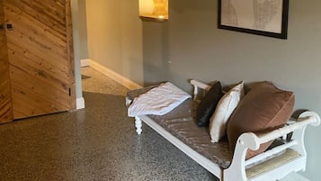 Ein Zimmer mit Holztür, einer gepolsterten Bank, einem gerahmten Bild an der Wand und einem Teppich mit Struktur.
