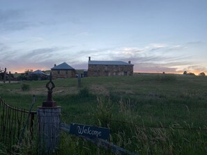 A rural landscape with a stone building and a wooden fence with a 'Welcome' sign.